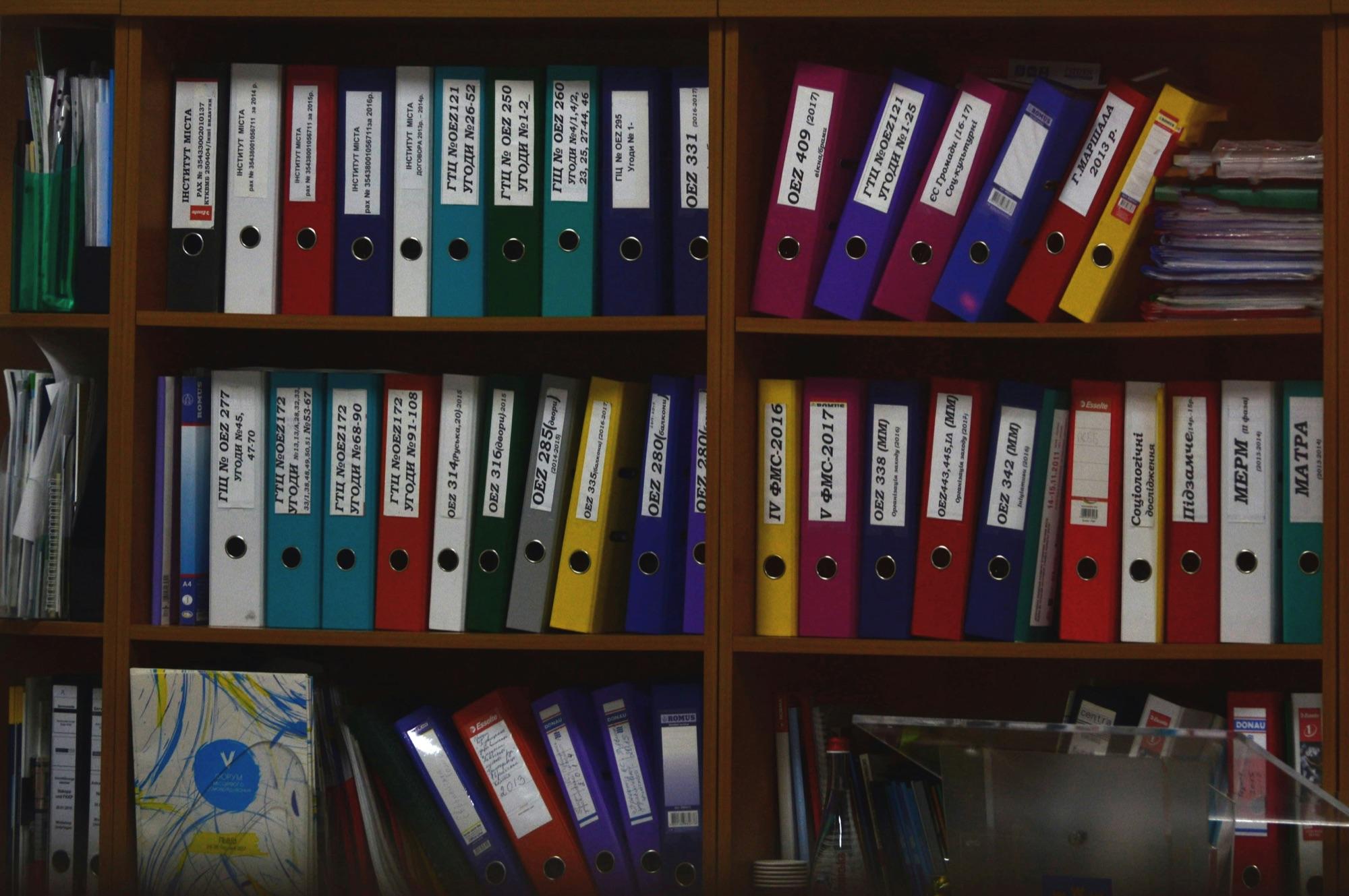 Office shelves packed edge to edge with labeled binders and box files